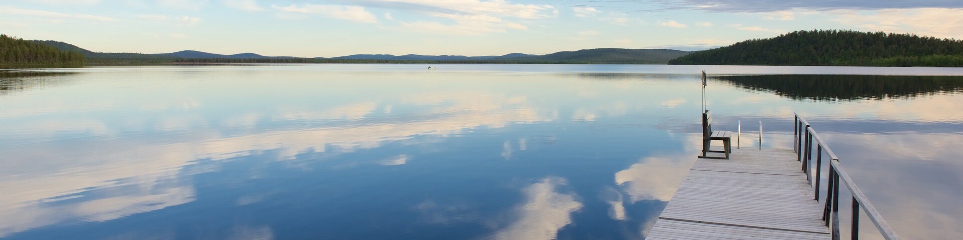 A calm lake with a wooden dock extending into the water, surrounded by forested hills.