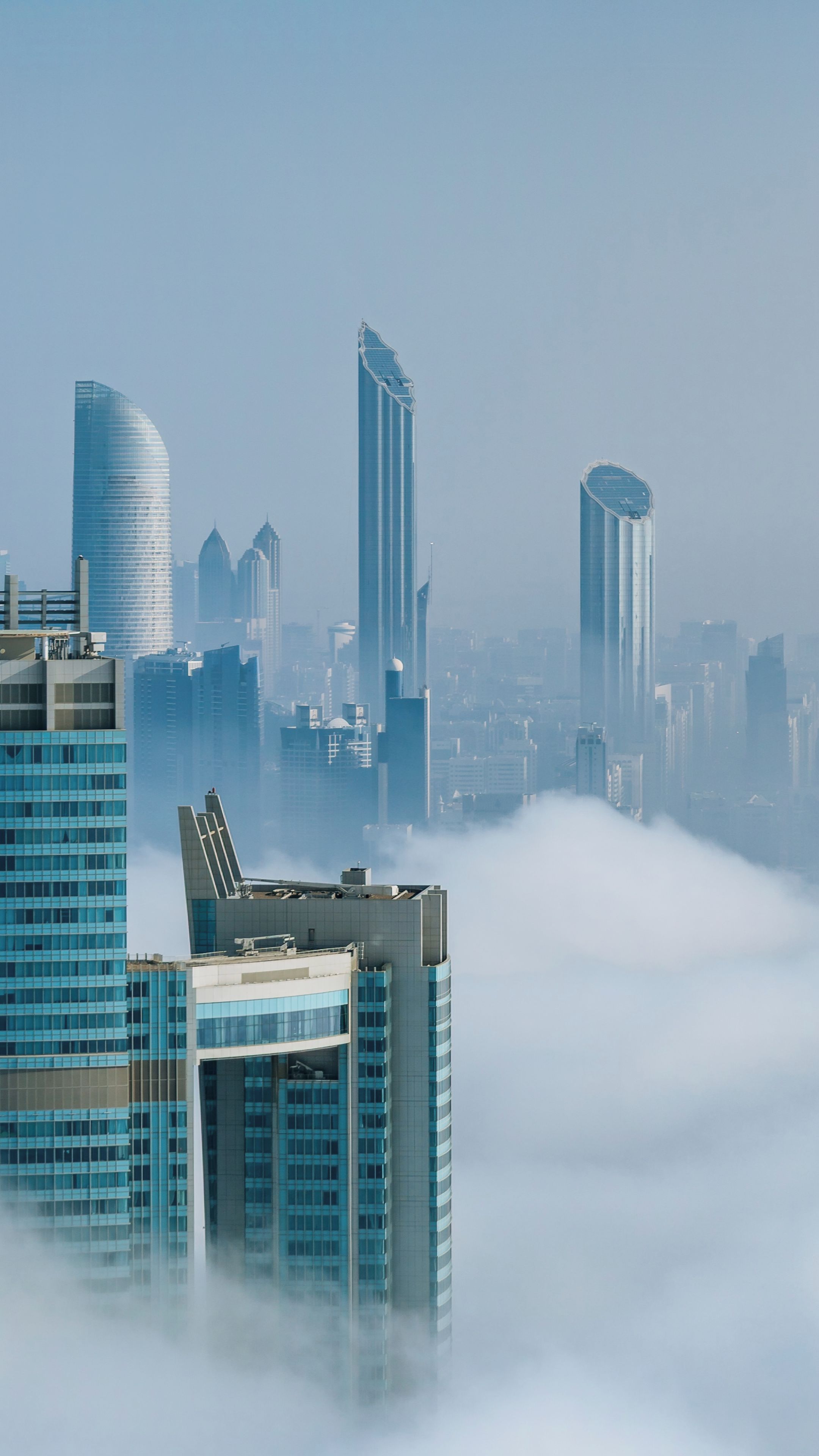 A cityscape with modern skyscrapers and a layer of fog or mist at the base.