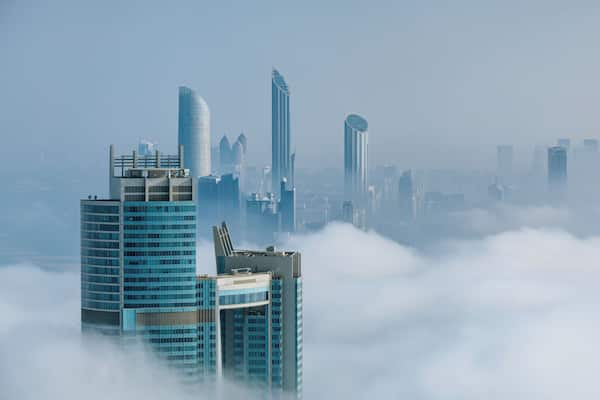 A city skyline with modern skyscrapers partially obscured by clouds.