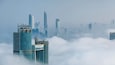 A city skyline with modern skyscrapers partially obscured by clouds.