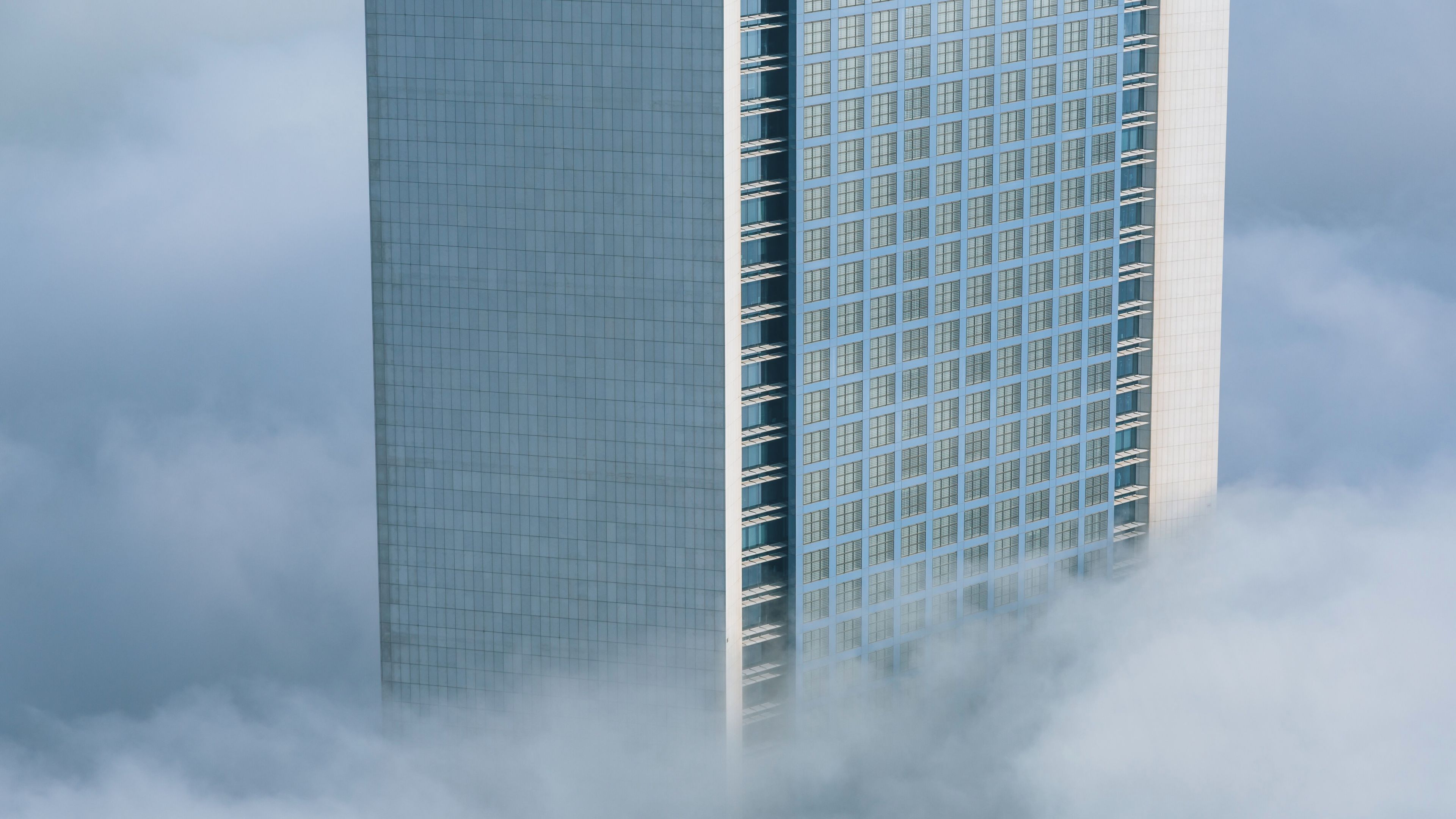 A tall skyscraper with a grid-like facade, partially obscured by clouds.