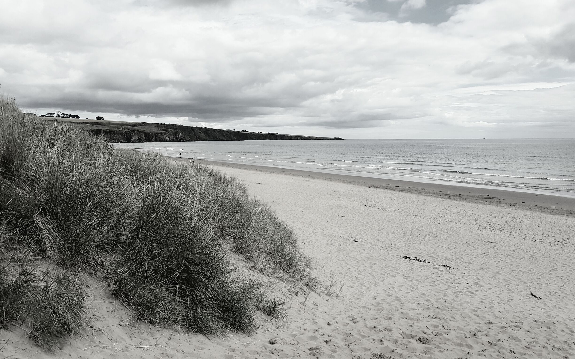 A beach with sand dunes and a cloudy sky.