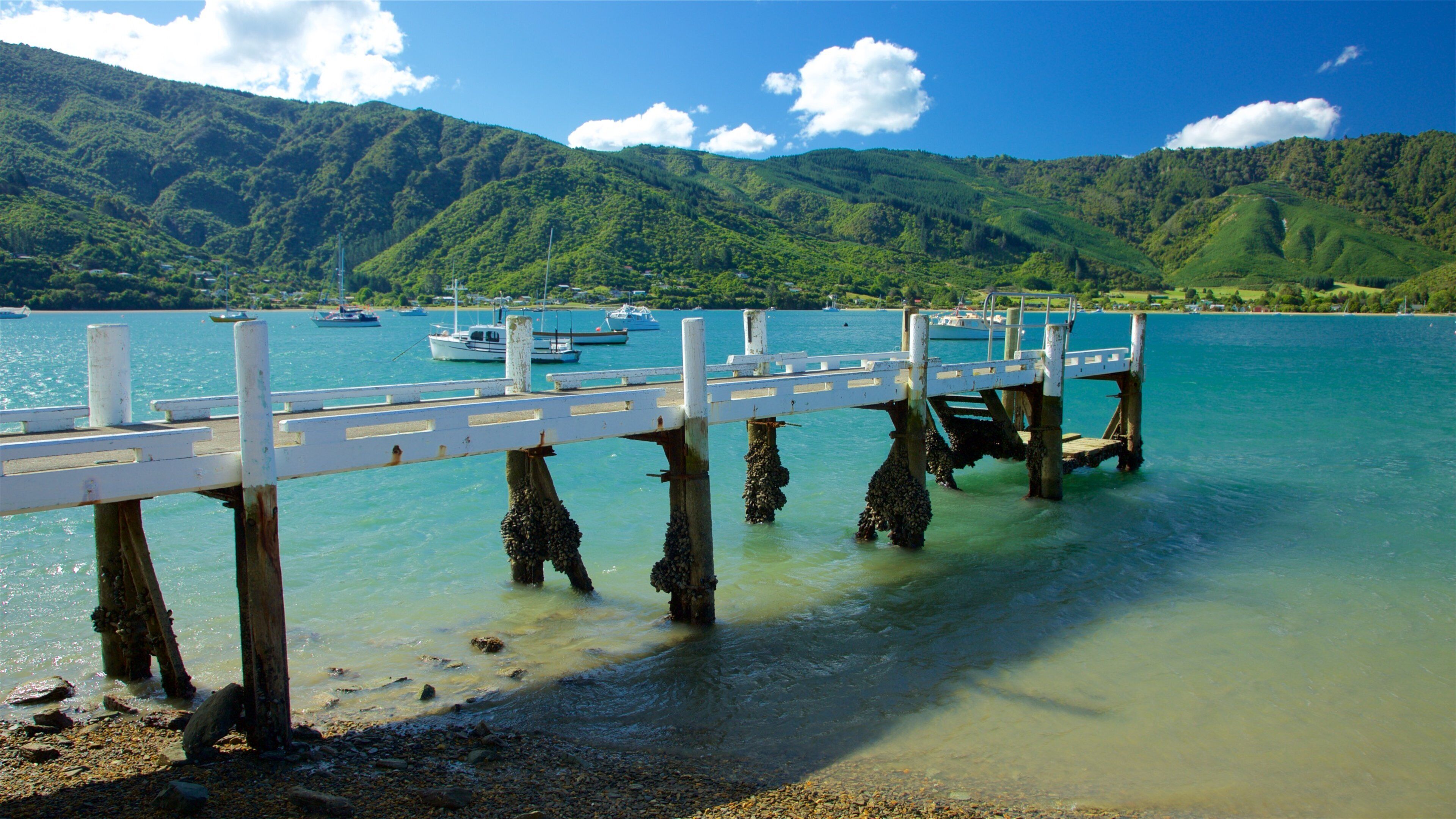 A pier extending into a calm lake with boats docked, surrounded by lush green hills.