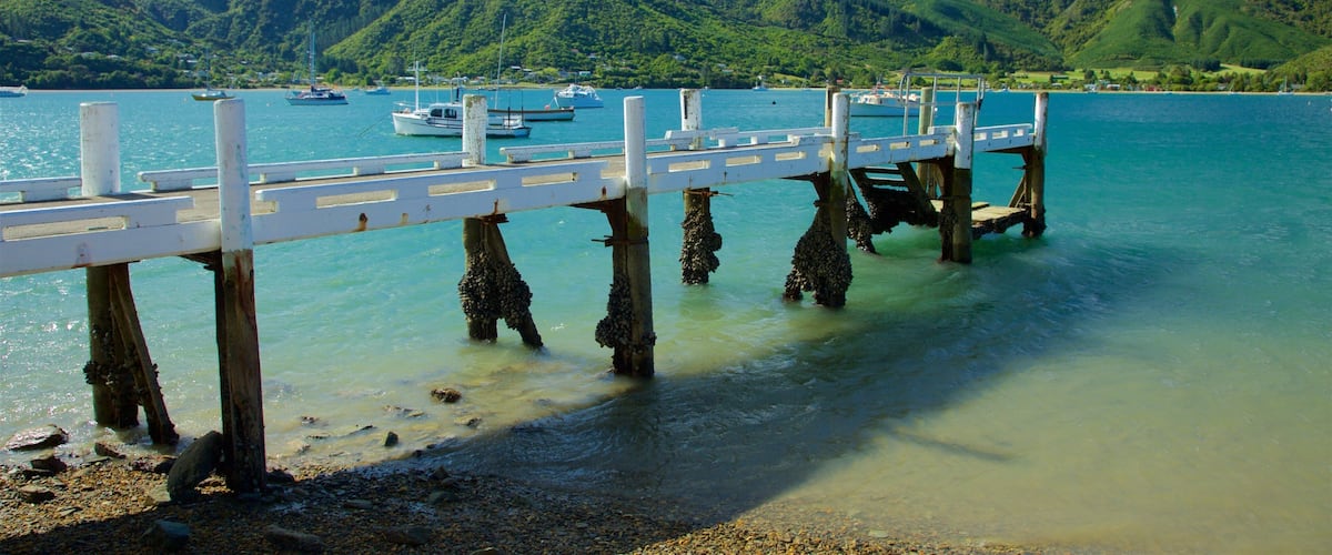 A pier extending into a calm lake with boats docked, surrounded by lush green hills.