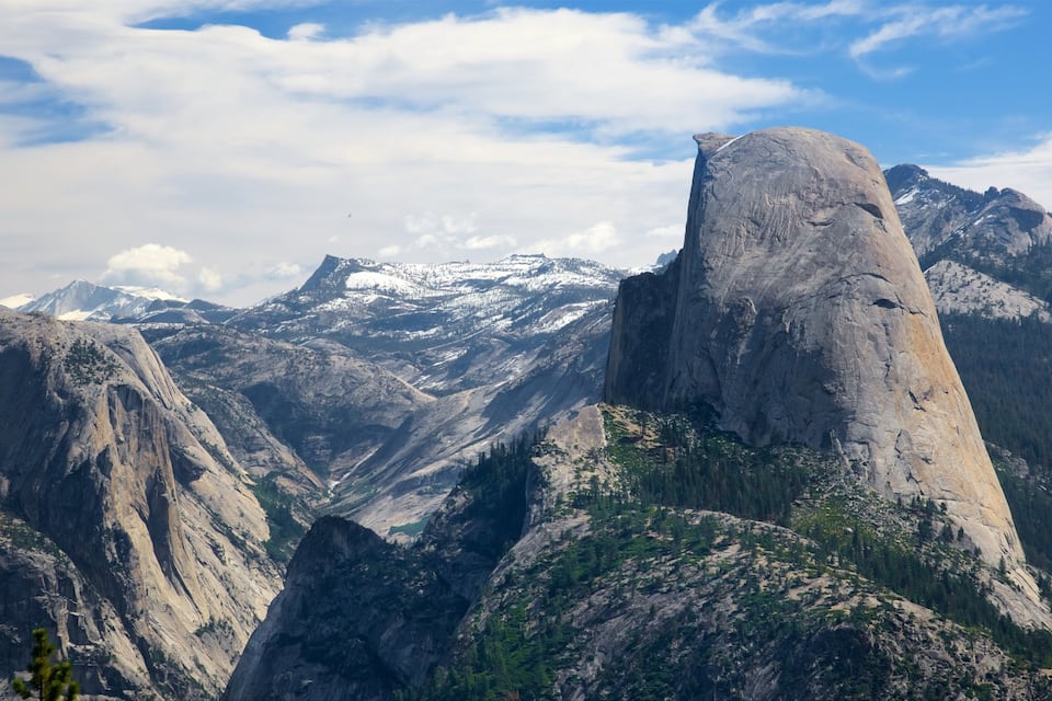 A mountain landscape with a prominent rock formation, snow-capped peaks, and a valley.