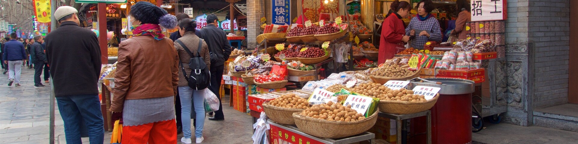 Um mercado de rua movimentado com diversos quiosques vendendo frutas, nozes e outros produtos.