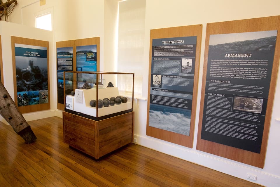 An exhibit with maritime artifacts, including anchors and cannons, displayed in a wooden case.