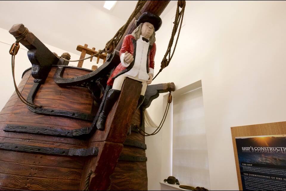 Um leme de navio e uma figura vestida com traje histórico.