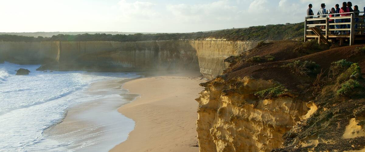 A coastal cliff with a sandy beach and a viewing platform with people.