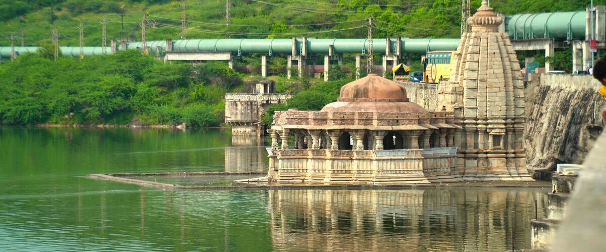 A temple on a riverbank with a green train in the background.