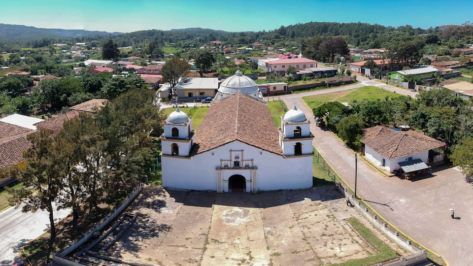 A white church with a dome and bell towers, surrounded by residential buildings and greenery.