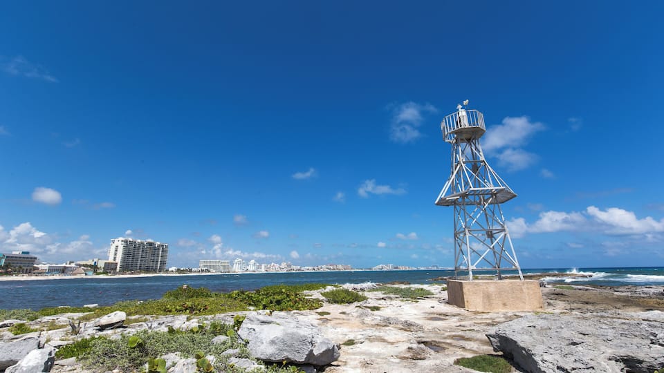 A coastal landscape with a lighthouse, rocky shore, and a distant city skyline.