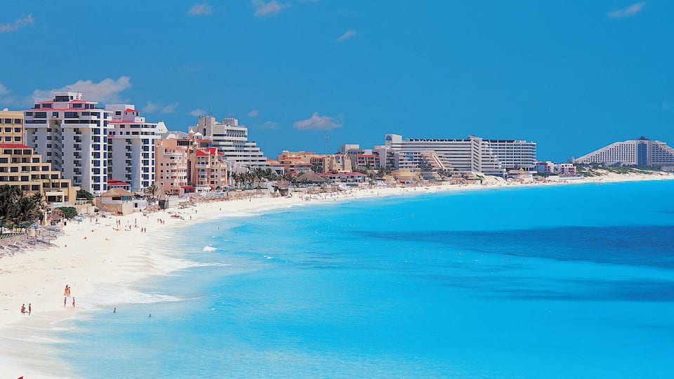 A coastal city with a long sandy beach, clear blue waters, and a skyline of high-rise buildings.
