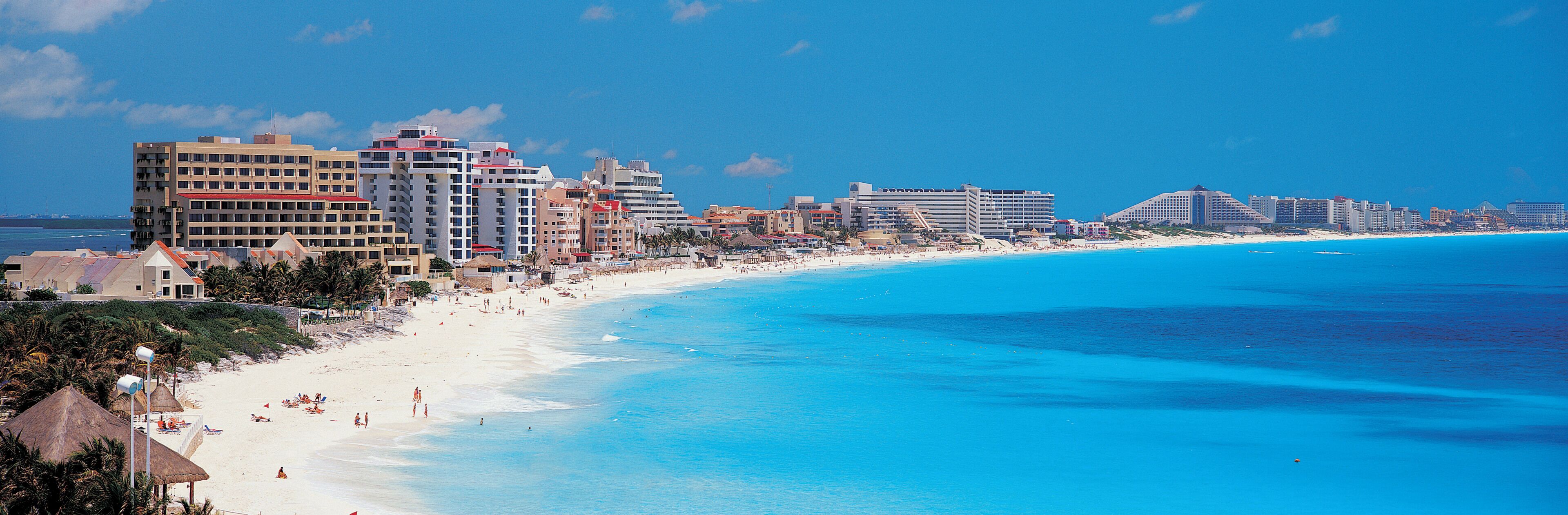 A coastal city with a long sandy beach, clear blue waters, and a skyline of high-rise buildings.