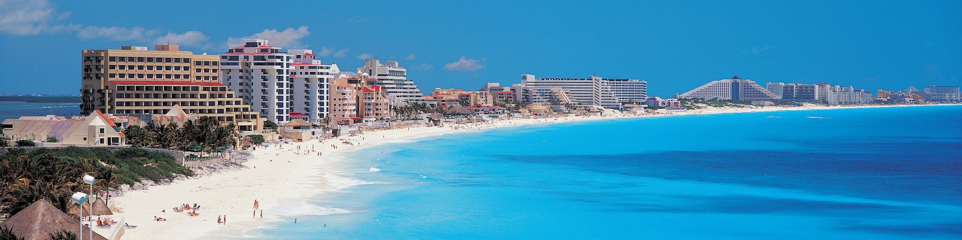A coastal city with a long sandy beach, clear blue waters, and a skyline of high-rise buildings.