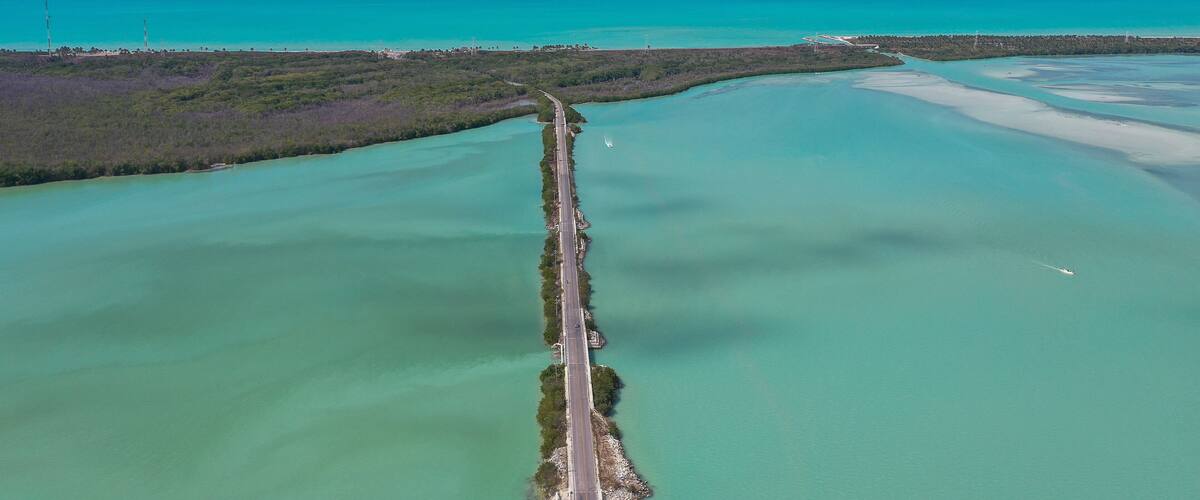 An aerial view of a coastal road with turquoise waters and a clear sky.