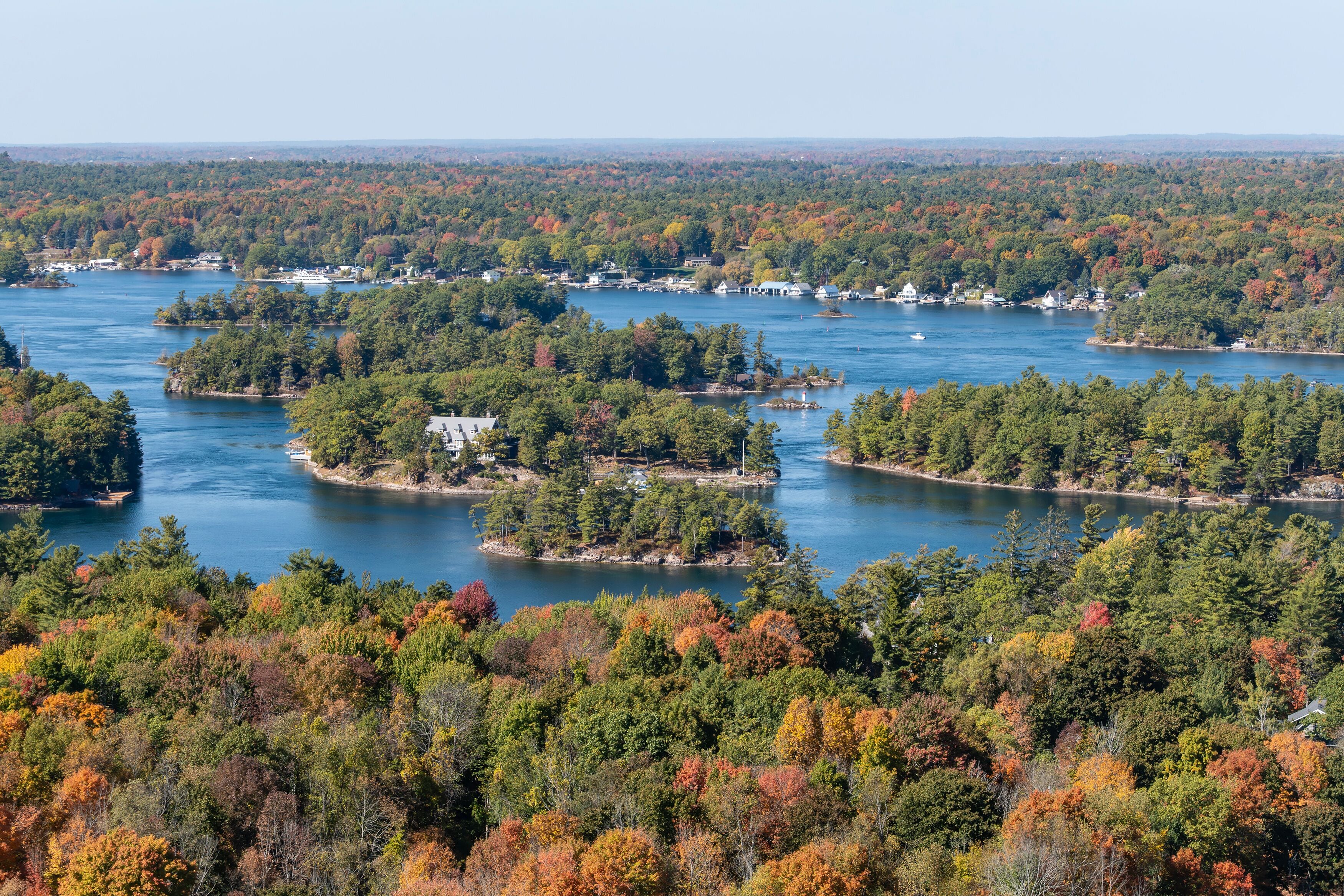A lake surrounded by dense forest with autumn foliage, small islands, and clear skies.