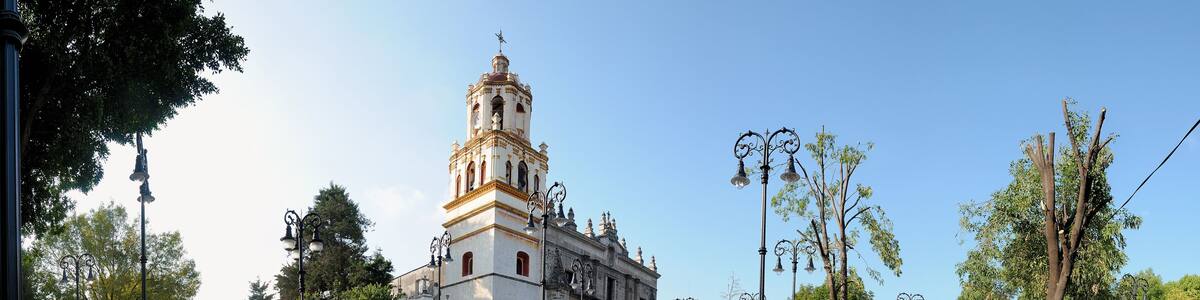 A historic church with a bell tower, a wet plaza, and surrounding trees.