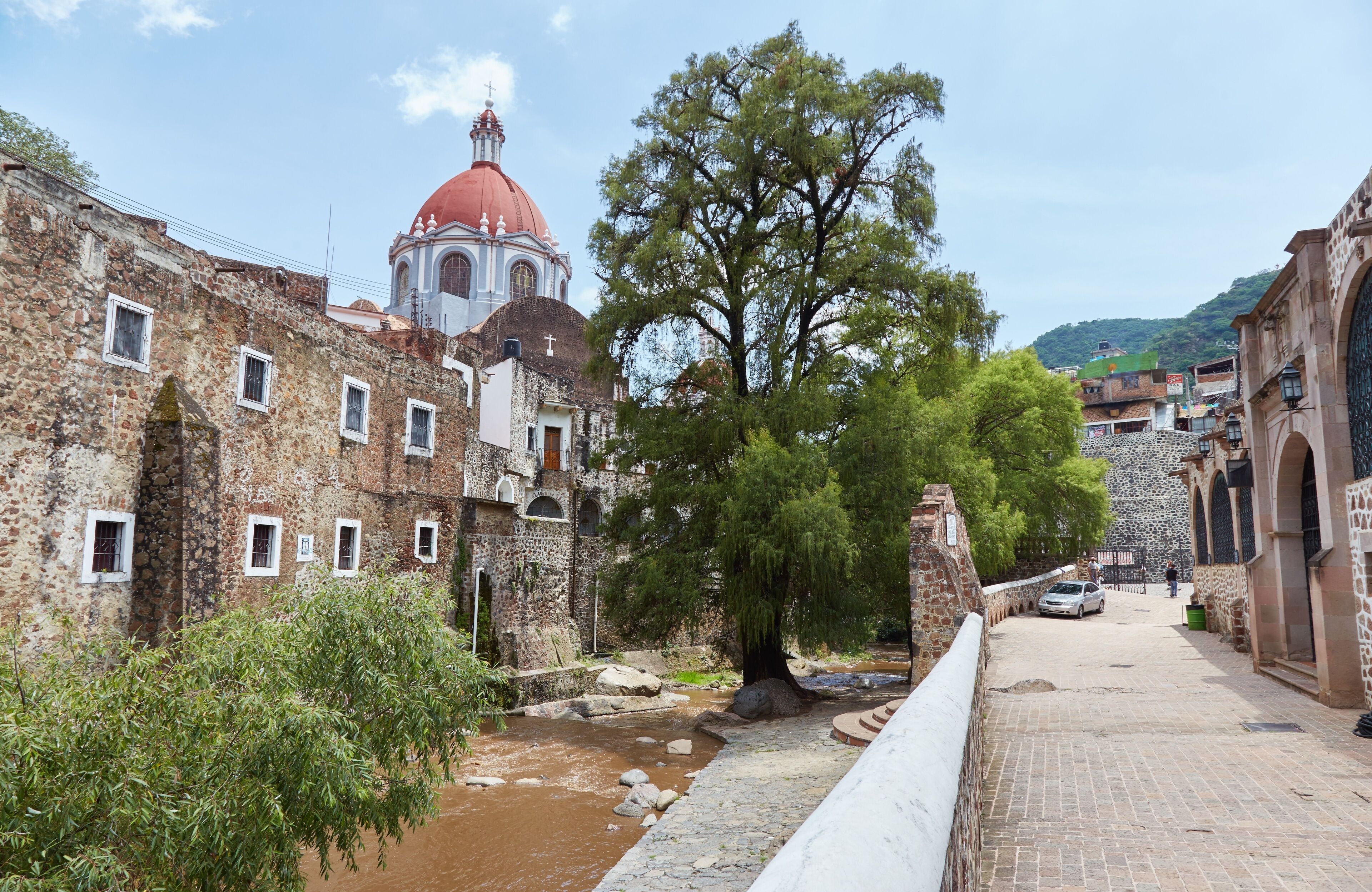 A historic town with stone buildings, a river, and a prominent church with a red dome.