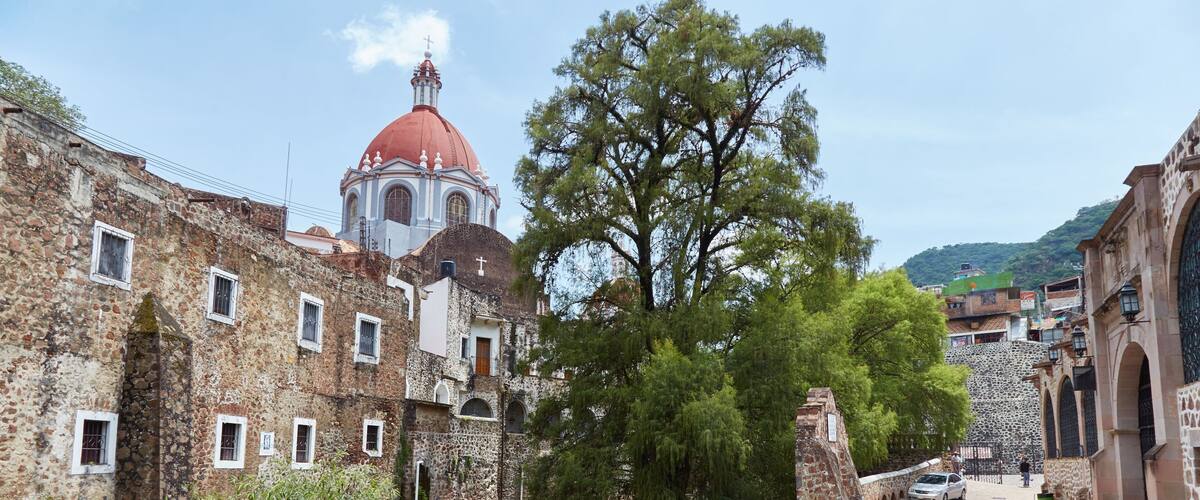 A historic town with stone buildings, a river, and a prominent church with a red dome.