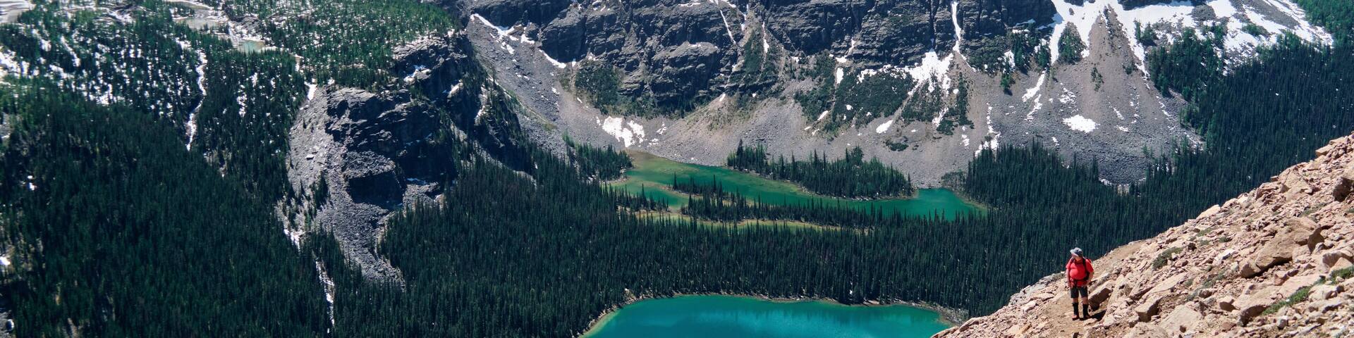 A mountainous landscape with a turquoise lake, snow-capped peaks, and dense forests.