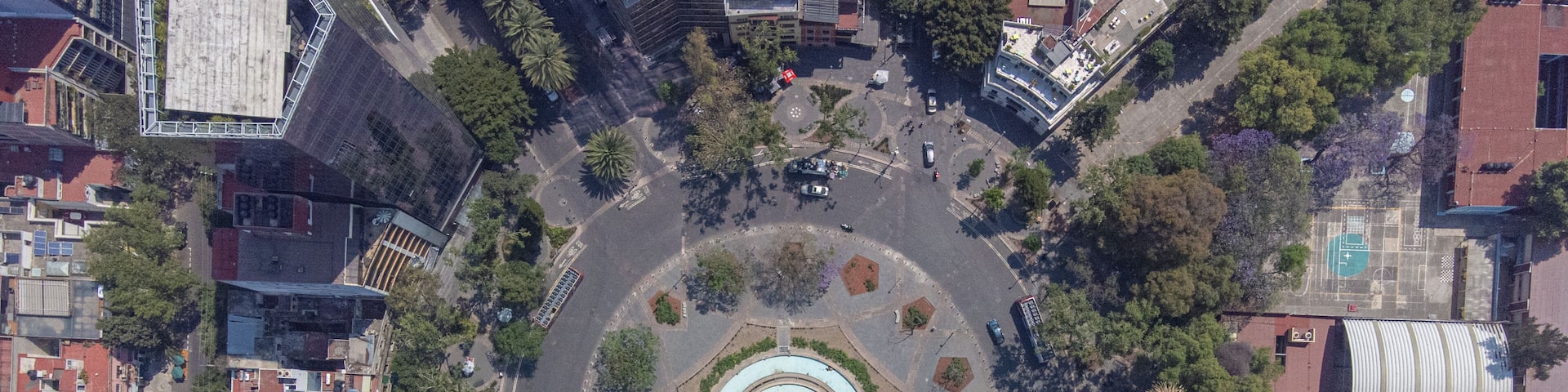 An aerial view of a city with a central circular plaza, surrounded by buildings and trees.