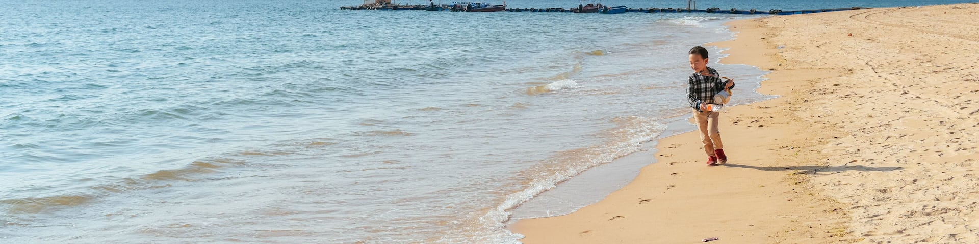 A sandy beach with gentle waves, a distant boat, and a clear sky.