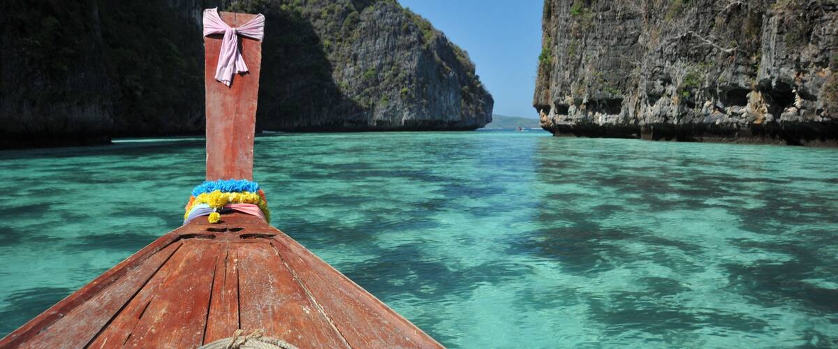 A wooden boat with a pink bow, tied to a rocky shore with clear turquoise water.