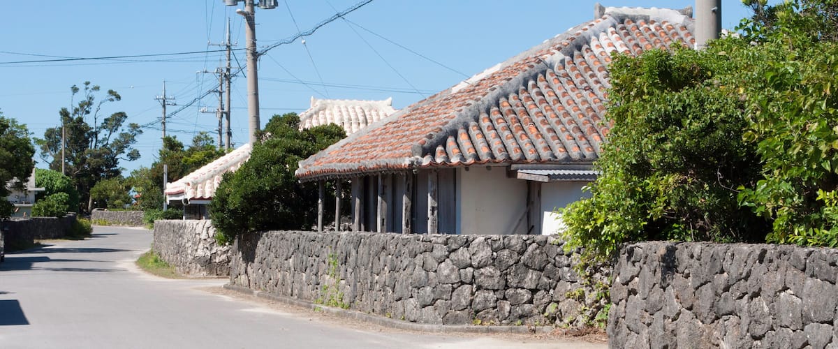 A traditional house with a tiled roof, a stone wall, and a clear blue sky.