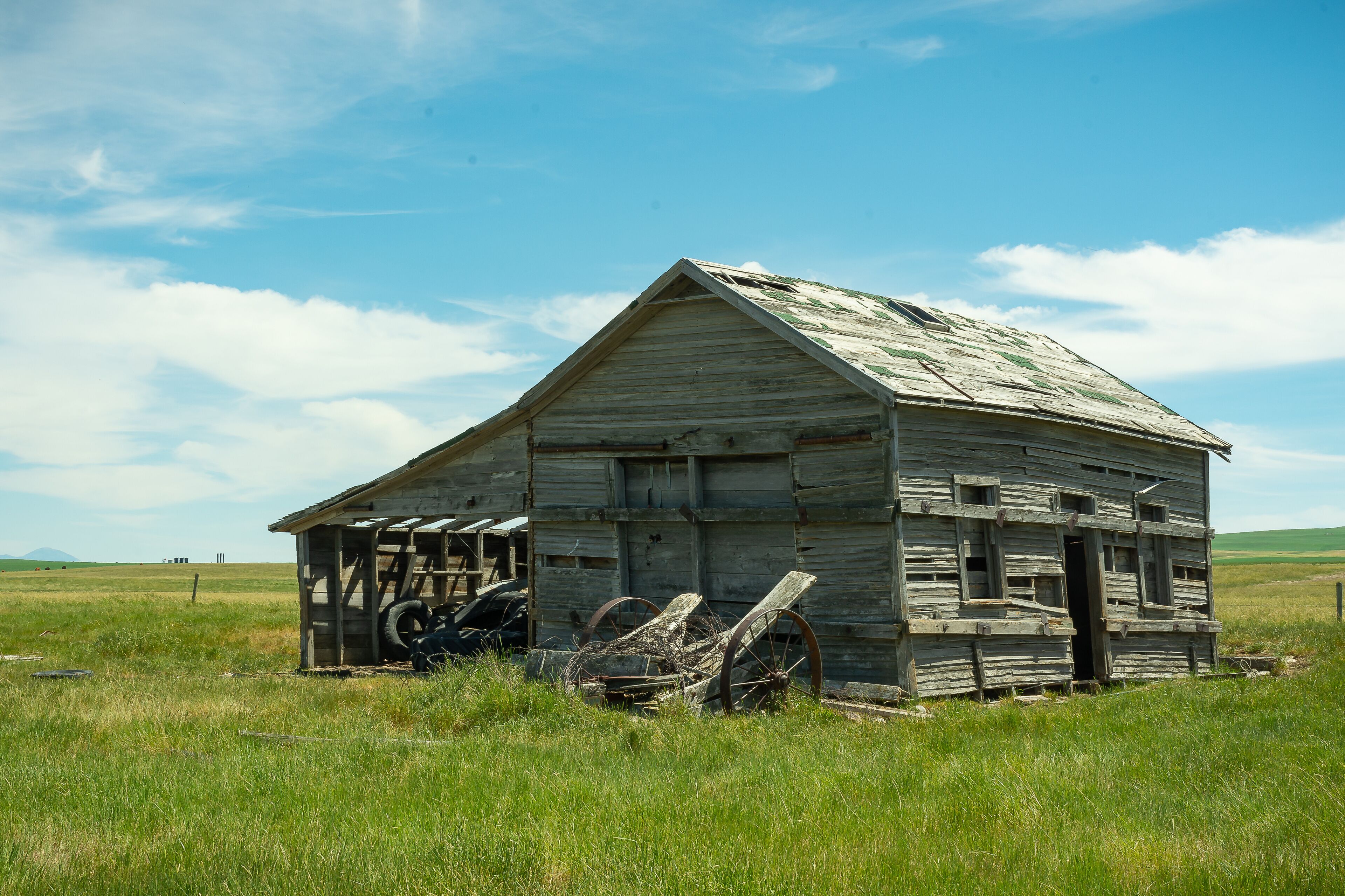 An old wooden barn with a weathered roof and a large wheel in the foreground.