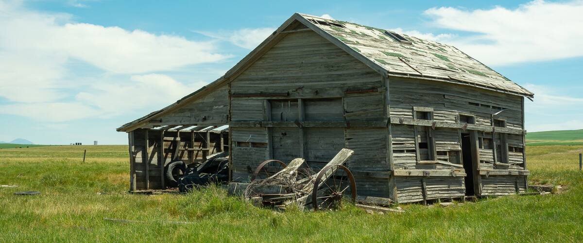 An old wooden barn with a weathered roof and a large wheel in the foreground.