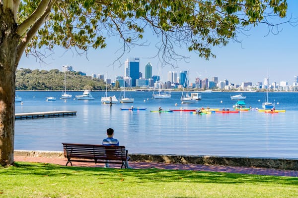 Ein Park am Wasser mit einer Bank, einer Stadtansicht und verschiedenen Booten auf dem Wasser.