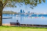 A waterfront park with a bench, a city skyline, and various boats on the water.