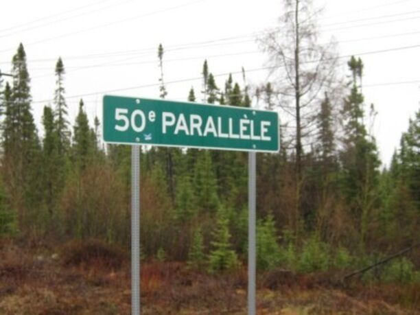 A street sign reading "50e PARALLELE" in a forested area.