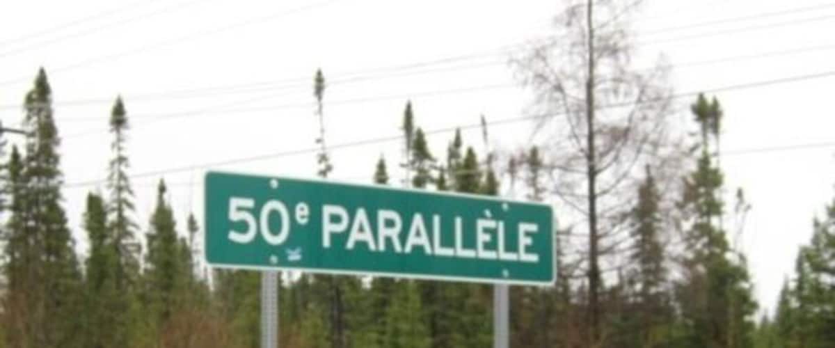 A street sign reading "50e PARALLELE" in a forested area.
