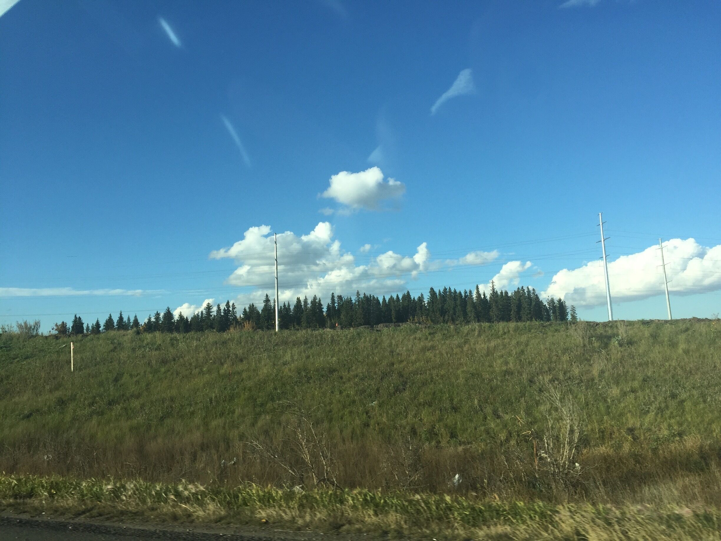 A grassy hill with a clear blue sky and scattered clouds.