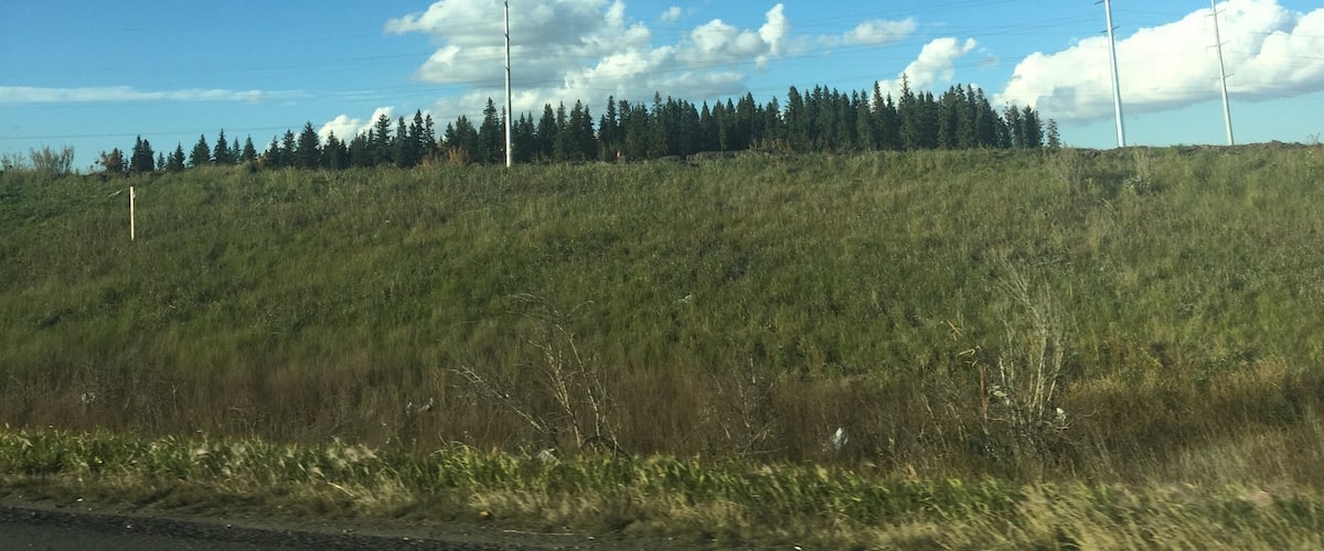 A grassy hill with a clear blue sky and scattered clouds.