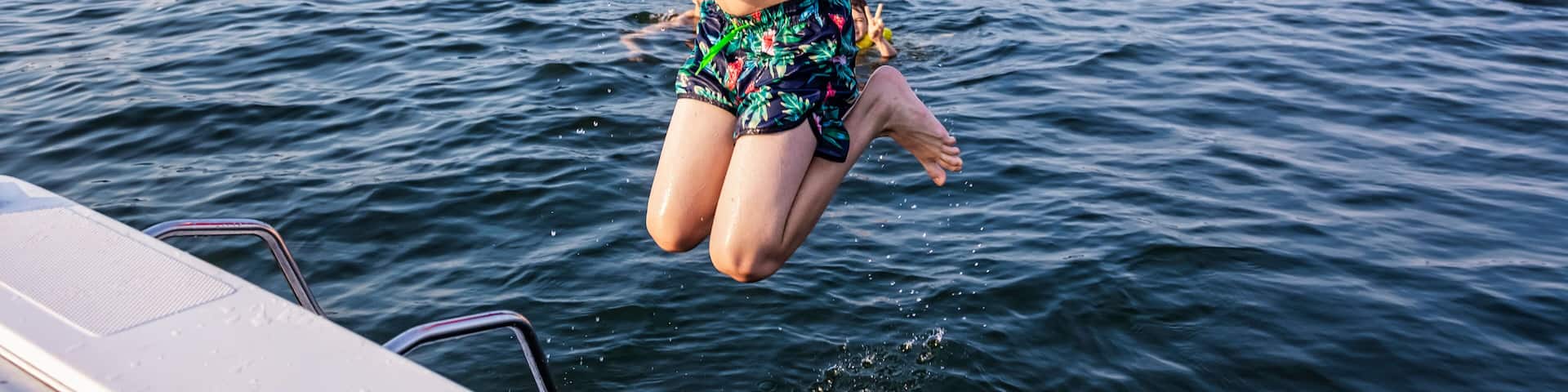 Young boy jumping off a boat and swimming in a lake with a lifejacket, Lac Ste. Anne; Alberta Beach, Alberta, Canada