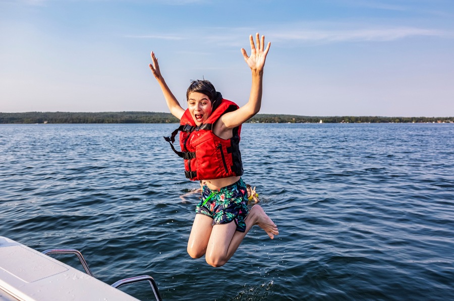 Young boy jumping off a boat and swimming in a lake with a lifejacket, Lac Ste. Anne; Alberta Beach, Alberta, Canada