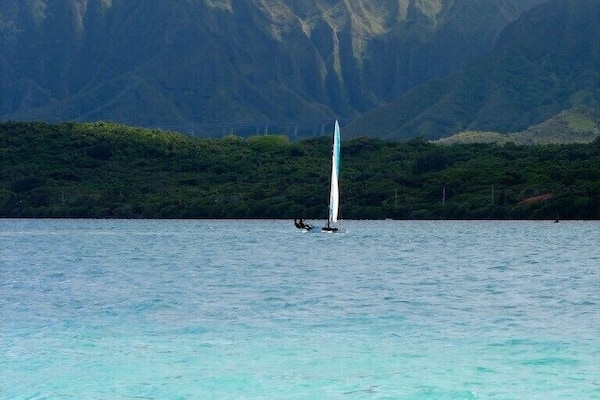 A sailboat on turquoise water with a mountain in the background.