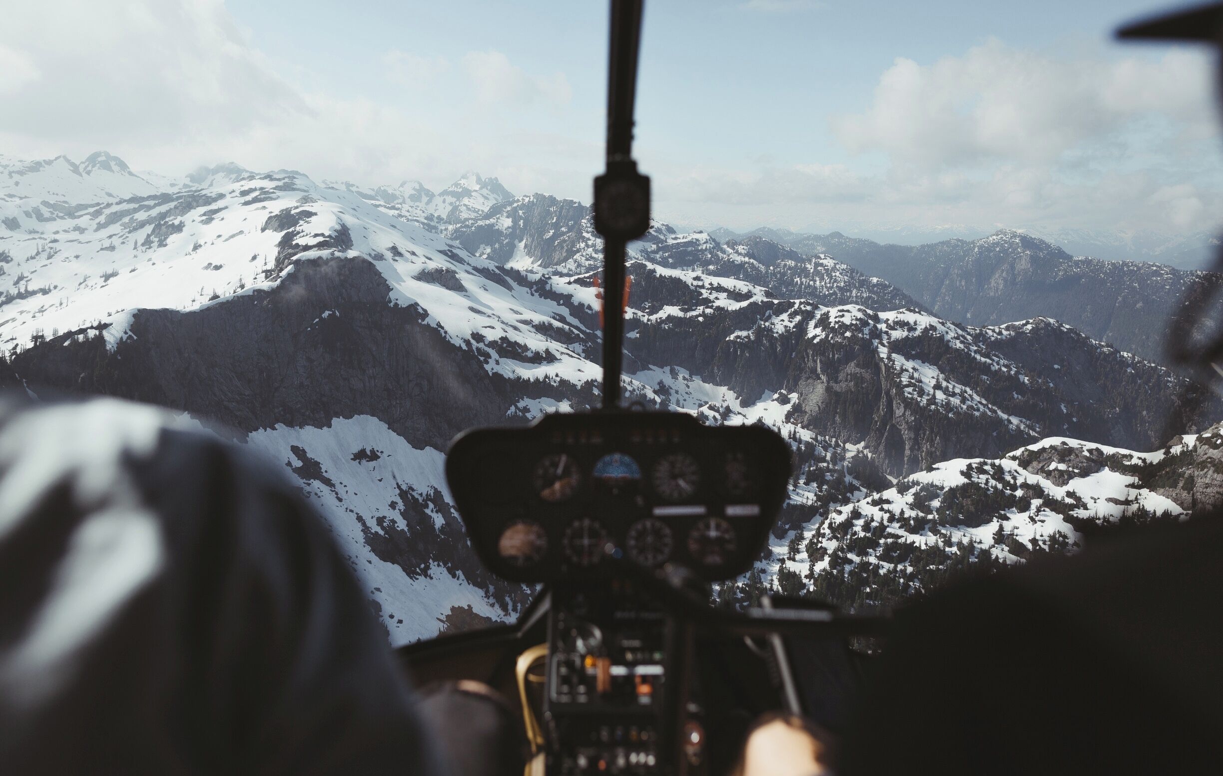 A helicopter's cockpit with a snowy mountain range in the background.