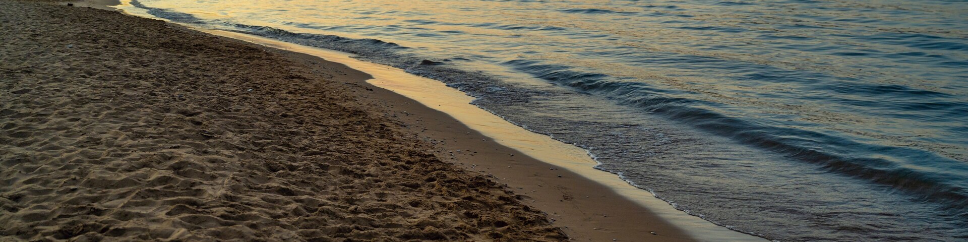 A beach with sand and water, a distant mountain, and a sunset.