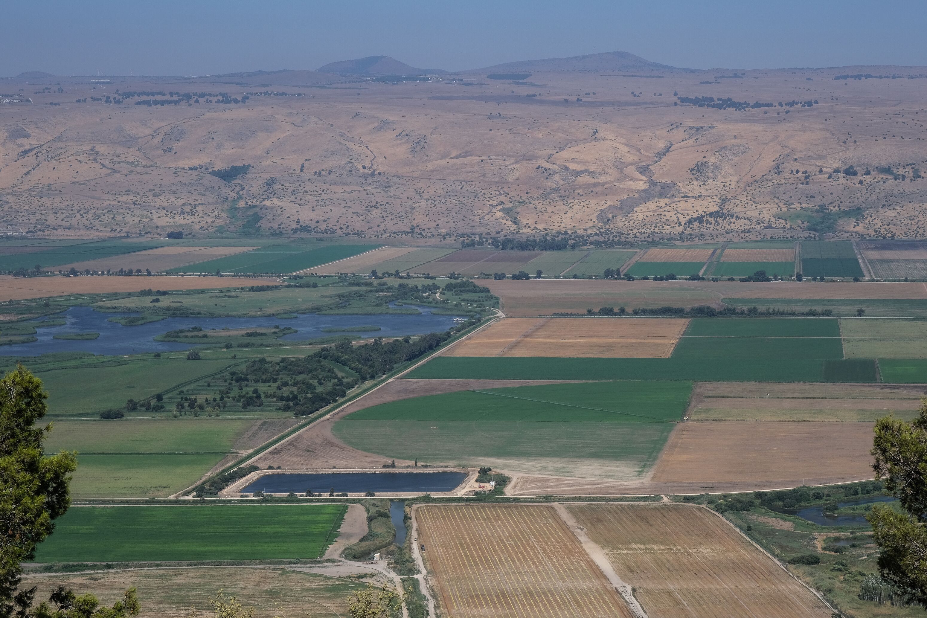 A vast agricultural landscape with terraced fields, a small body of water, and rolling hills in the background.