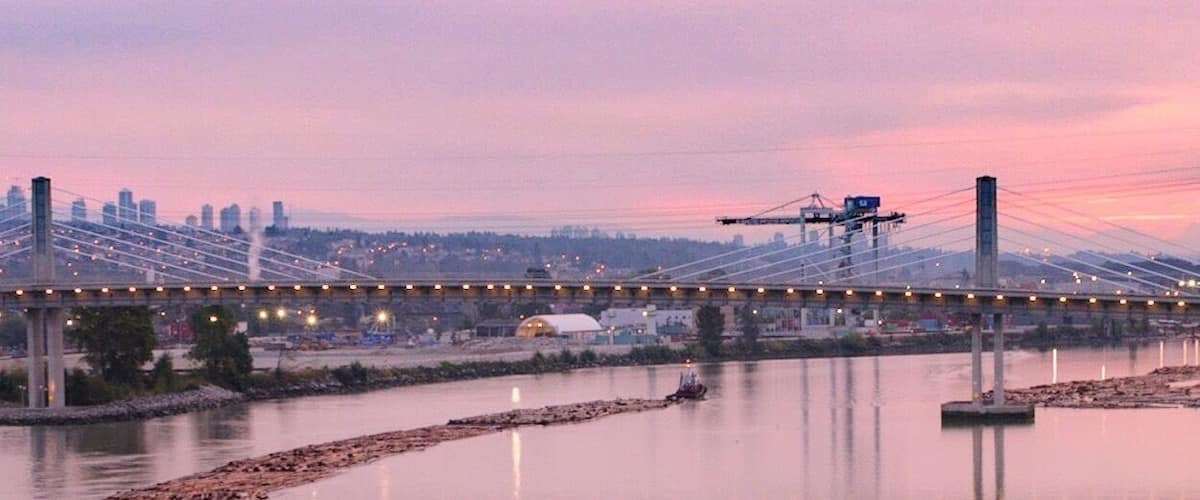 A river with a wooden breakwater and a tugboat. A bridge spans the river in the background.