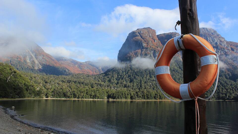 A lifebuoy attached to a wooden post by a lake with mountains in the background.