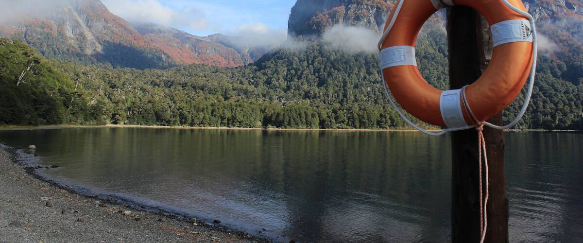 A lifebuoy attached to a wooden post by a lake with mountains in the background.
