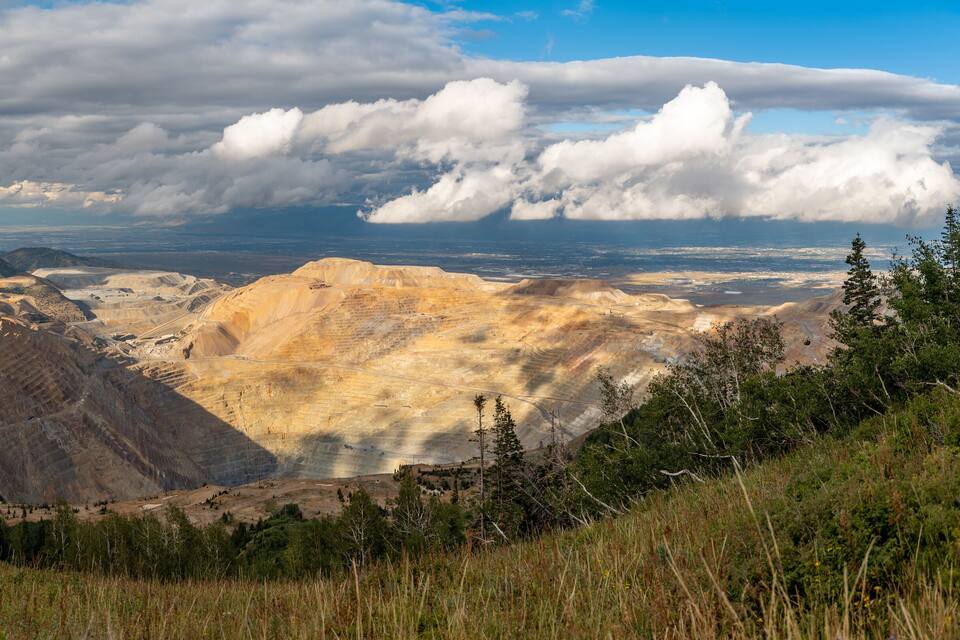 A mountainous landscape with a large open quarry and distant mountains under a cloudy sky.