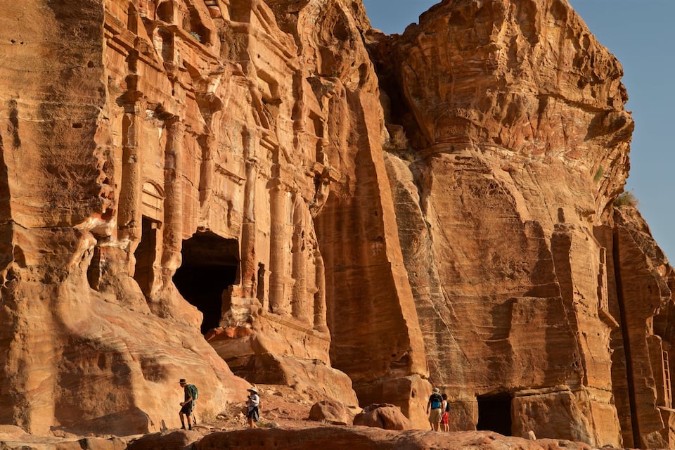 Uma grande formação rochosa de arenito com colunas esculpidas e a entrada de uma caverna.
