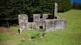 Ruinas de piedra con una chimenea, rodeadas de hierba y árboles.