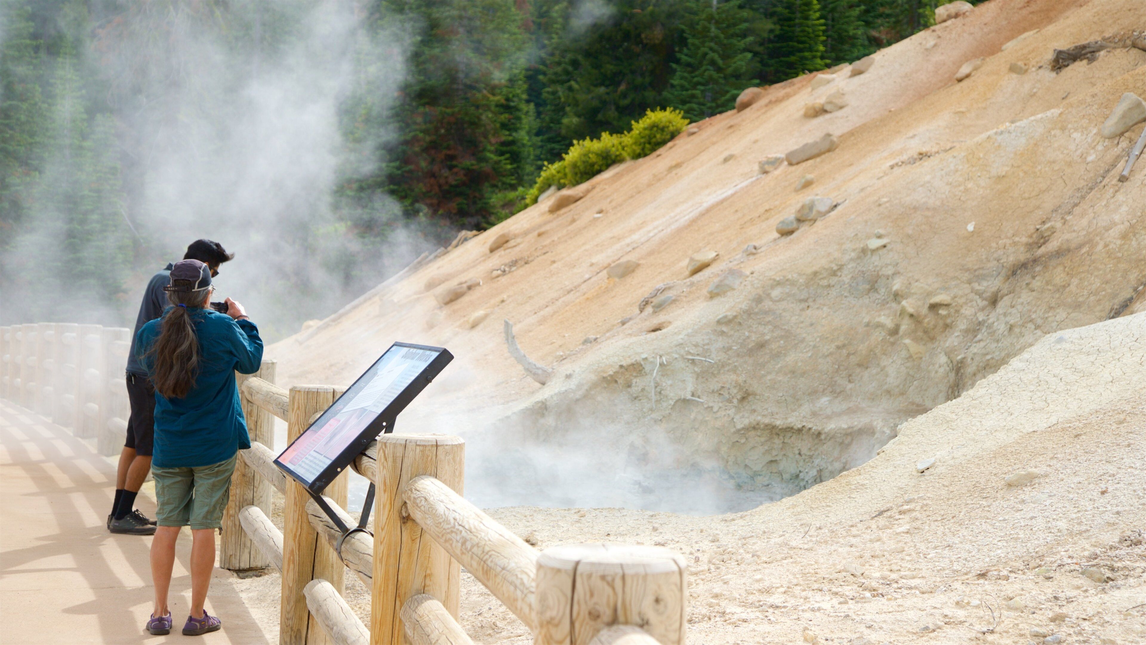 A wooden fence with a digital sign, a sandy slope, and a person taking a photo.